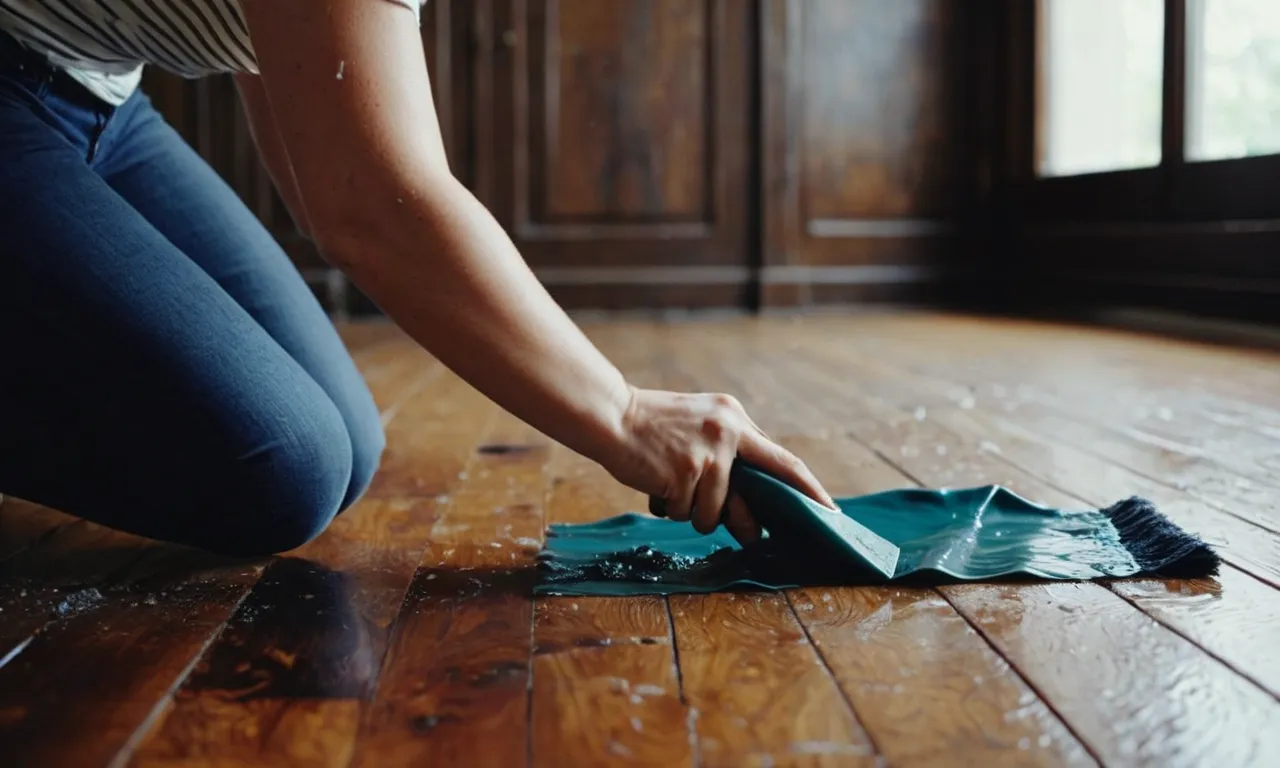 A photo showcasing a person carefully scraping off melted wax from a wooden floor using a plastic scraper, accompanied by a damp cloth ready to wipe away any residue.