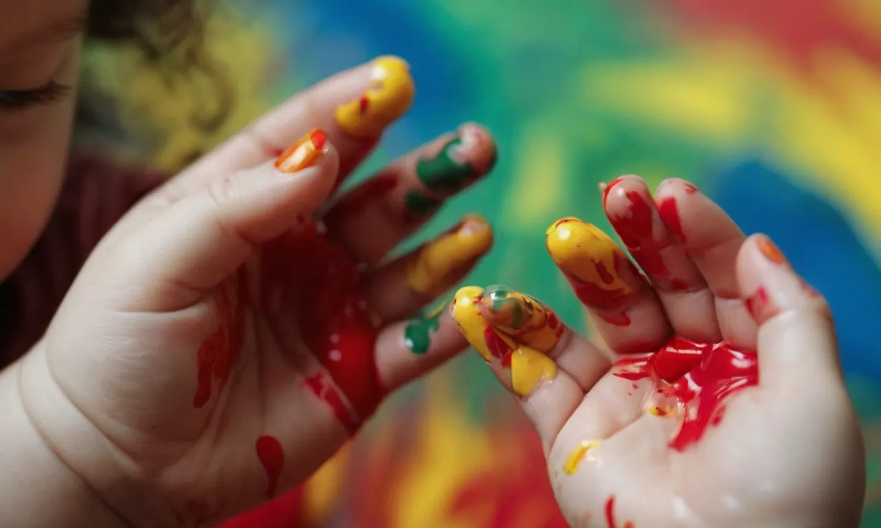A close-up photo capturing a baby's tiny hands playfully smeared with vibrant acrylic paint, showcasing their curiosity and innocence, while emphasizing the safety concerns surrounding the topic.